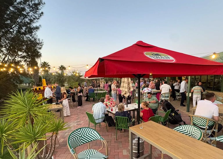 Outdoor event under a red tent with guests, tropical plants, and striped seating at dusk